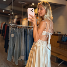 Load image into Gallery viewer, Model wearing Aurora Boutique Miami Anori maxi dress with open bust, tie back, and pleated skirt in a boutique setting