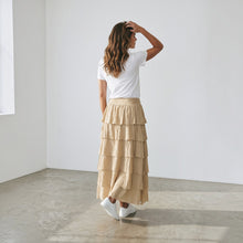 Load image into Gallery viewer, Model wearing Aurora Boutique Miami beige tiered cotton maxi skirt with a white t-shirt and sneakers, back view