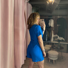 Load image into Gallery viewer, Model wearing a vibrant blue Aurora Boutique Miami pocketed button-up romper in a boutique dressing room mirror selfie