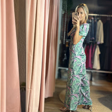 Load image into Gallery viewer, Aurora Boutique Miami model wearing a Cite floral jumpsuit with green palm leaf print on a light purple background