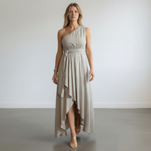 Load image into Gallery viewer, Model wearing an Aurora Boutique Miami cocoa one-shoulder flowy dress with a high-low hem and waist tie