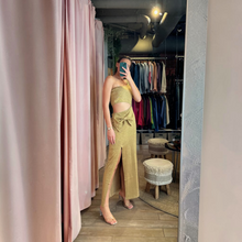 Load image into Gallery viewer, Model wearing a gold lurex one-shoulder crochet maxi dress with a waist cutout and bow detail by Aurora Boutique Miami