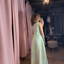 Load image into Gallery viewer, Model wearing a mint green Aurora Boutique Miami sleeveless maxi dress with a tied back detail in a boutique setting