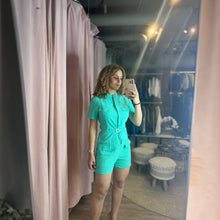 Load image into Gallery viewer, Model wearing a bright turquoise Aurora Boutique Miami button-up romper with pockets and a belt in a mirror selfie.