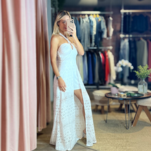 Load image into Gallery viewer, Model wearing a white lace Carla Romper Dress by Aurora Boutique Miami with a halter neckline and high leg slit.