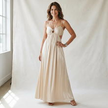 Load image into Gallery viewer, Model wearing an Aurora Boutique Miami Anori maxi dress in champagne with an open bust, ring detail, and tie back.
