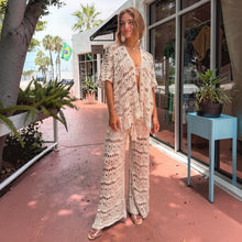 Load image into Gallery viewer, Model wearing Aurora Boutique Miami beige crochet three-piece set with open cardigan and wide-leg pants outdoors.
