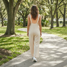 Load image into Gallery viewer, Aurora Boutique Miami Helena linen wide leg jumpsuit in beige worn by a woman walking on a park path
