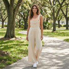 Load image into Gallery viewer, Model wearing an Aurora Boutique Miami beige linen wide leg jumpsuit with a peach tank top in a park setting
