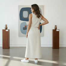 Load image into Gallery viewer, Model wearing an Aurora Boutique Miami beige sleeveless skirt set with white sneakers in an art gallery setting.
