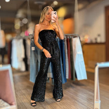 Load image into Gallery viewer, Aurora Boutique Miami Alegria tube belted sequin jumpsuit in black worn by a model in a clothing store mirror selfie.
