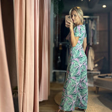 Load image into Gallery viewer, Aurora Boutique Miami model wearing a Cite floral jumpsuit with green palm leaf print on a light purple background
