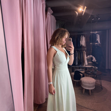 Load image into Gallery viewer, Aurora Boutique Miami Kara Minty tied maxi dress in light green worn by a woman taking a mirror selfie in a boutique.
