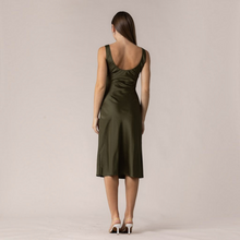 Load image into Gallery viewer, Back view of a model wearing an Aurora Boutique Miami olive green satin midi dress with a scoop back design.
