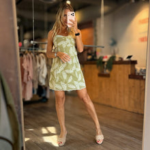 Load image into Gallery viewer, Aurora Boutique Miami Amaia mini dress in sage green with white leaf print, worn by a model in a boutique mirror.
