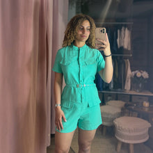 Load image into Gallery viewer, Model wearing a bright turquoise Aurora Boutique Miami button-up romper with front pockets and a matching belt.
